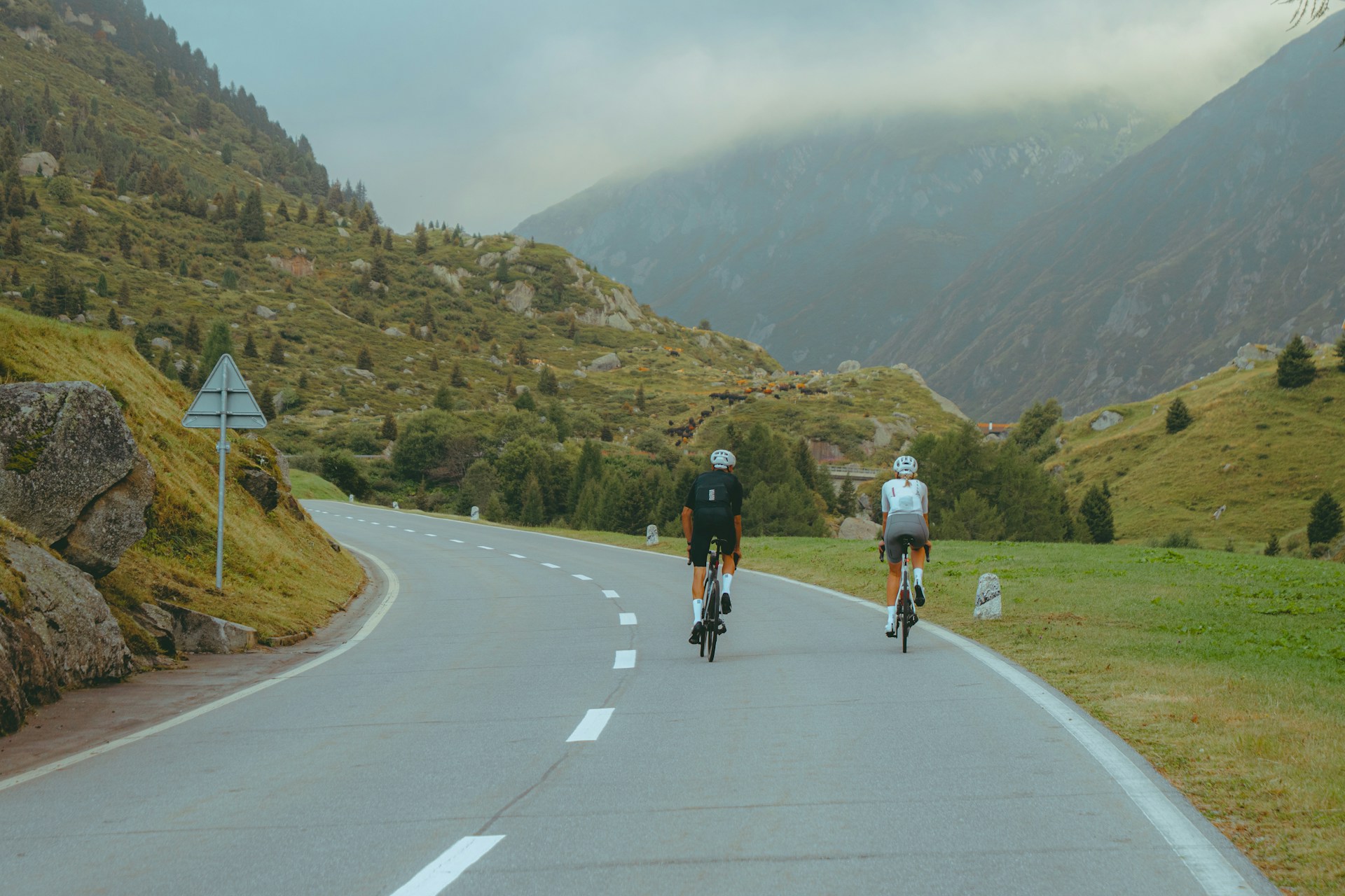 Two cyclists riding an open mountain road in the Swiss Alps